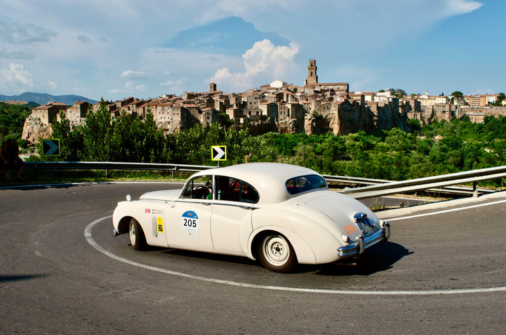 De kolossale Jaguar Mark VII van equipe Dino Bonatti en Monica Gandolfi met op de achtergrond Pitigliano.
